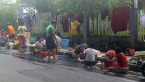 Warga memanfaatkan air got yang meluber ke baju jalan untuk mencuci (foto beritamanado)