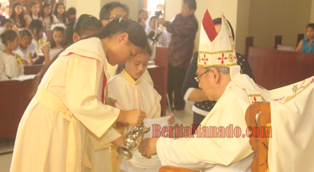 Fabiola Lenak (kiri) saat menuangkan air ke tangan Uskup Manado Mgr. Joseph Theodorus Suwatan MSC
