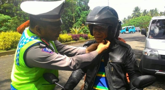 Petugas membantu memasangkan helm kepada pengendara kendaraan bermotor.