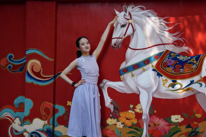 Blogger Tionghoa-Amerika Zhu Xirui, atau Sherry Zhu, berpose untuk difoto di depan mural bergambar kuda di Jalan Huanggongdong di tepi Danau Cuihu di Kunming, Provinsi Yunnan, China barat daya, pada 24 April 2026. (Xinhua/Chen Xinbo)