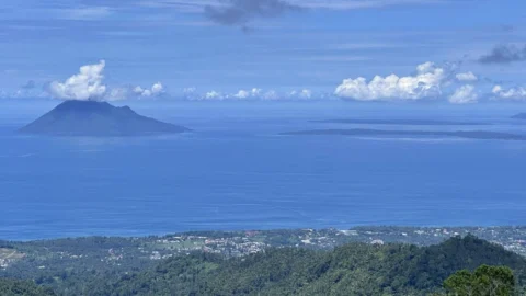 Pemandangan Teluk Manado dari Puncak Agotey di Kecamatan Mandolang, Kabupaten Minahasa dengan laut biru, perbukitan hijau, dan langit cerah.