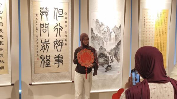 Seorang pengunjung berpose untuk difoto di sebuah pameran kaligrafi dalam Perayaan Hari Bahasa Mandarin Internasional di Landmark Pluit, Jakarta, pada 19 April 2026. (Xinhua/Abdul Azis Said)